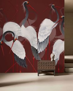 two white cranes are standing in front of a red wall with black and white designs