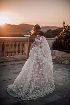 a woman in a wedding dress is standing on a balcony with the sun setting behind her