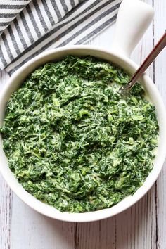 a white bowl filled with spinach on top of a wooden table next to a striped napkin