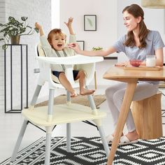 a woman sitting at a table with a baby in a high chair and another child reaching up