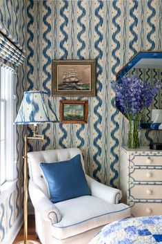 a bedroom decorated in blue and white with a chair, bed, dresser and mirror