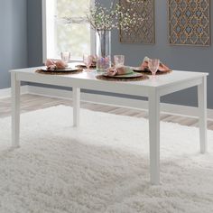 a white table with two place settings on it in front of a blue wall and window