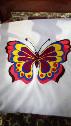 a colorful butterfly is sitting on top of a white sheet with red, yellow and blue designs