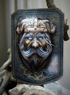 a metal plaque with an image of a man's face in the center, on top of driftwood