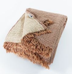 a brown and tan blanket folded on top of each other with fringes around the edges