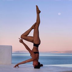 a woman doing a handstand in front of the ocean with her legs crossed