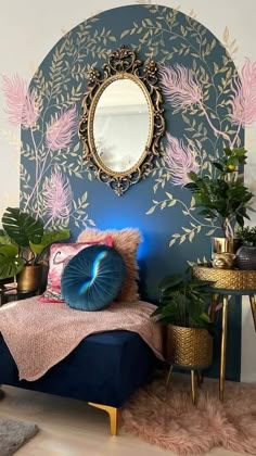 a bedroom with blue walls and pink flowers on the wall, gold mirror above the bed