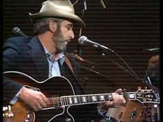 a man in a suit and hat playing an acoustic guitar while singing into a microphone