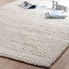 a white rug on top of a wooden floor next to a magazine rack and magazines