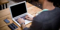 a man sitting at a wooden table using a laptop computer