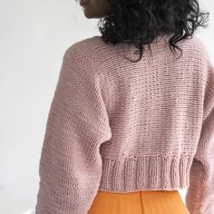 a woman with curly hair wearing a pink sweater and orange pleated skirt, looking off to the side