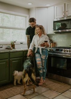 a man and woman are standing in the kitchen with their dog