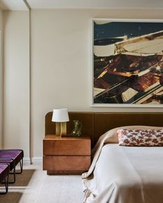 a bed sitting next to a painting on the wall in a room with white walls