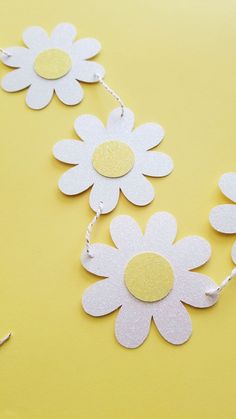 white paper flowers on a yellow background with scissors and thread to make them look like daisies