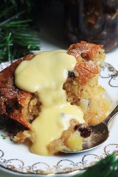 a piece of bread pudding on a plate with a spoon next to it and a pine tree in the background