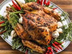 a roasted chicken on a platter with red peppers, garlic and parsley sprigs