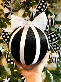 a hand holding an ornament in front of a christmas tree with black and white decorations