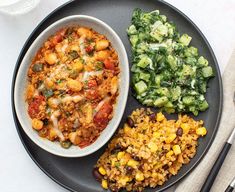 a black plate topped with rice, beans and vegetables next to a side of broccoli