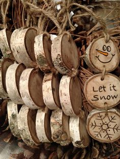 wood slices with snowman faces and words on them are hanging from the branches in front of a pile of pine cones