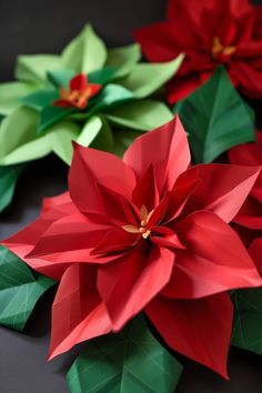 three paper poinsettis are sitting on a table with green and red leaves