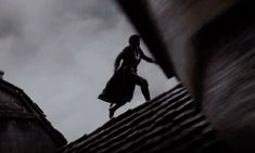 a woman standing on top of a roof next to a tall building under a cloudy sky