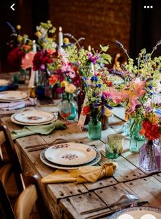 a wooden table topped with lots of plates and vases filled with different colored flowers