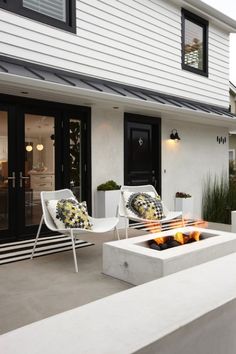 a fire pit sitting on top of a cement slab next to a white house with black doors