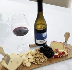 a bottle of wine, cheese and grapes on a cutting board next to a glass of red wine