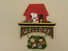 a welcome sign hanging from the side of a wall with a snoopy house on it