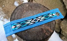 a blue beaded bracelet sitting on top of a piece of wood next to snow