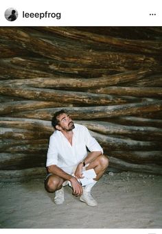 a man sitting in front of a pile of logs with his hands on his knees