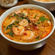 a bowl of soup with shrimp and other foods in it on a wooden table top