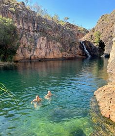 two people swimming in the water near a waterfall