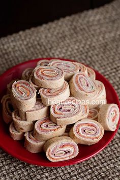 a red plate filled with rolled up rolls on top of a brown tablecloth covered floor