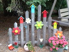 a wooden fence with flowers and bird houses on it, along with other garden decorations