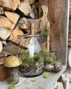 a candle is lit in a glass jar with moss and pine cones on a wooden table