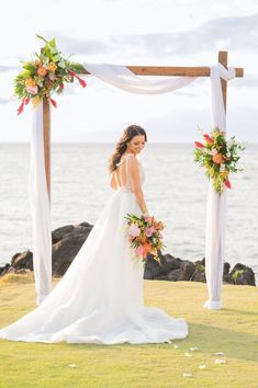 a woman in a wedding dress is standing under an arch with flowers and greenery