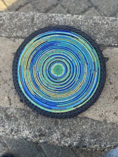 a blue and green plate sitting on top of a stone wall next to a person