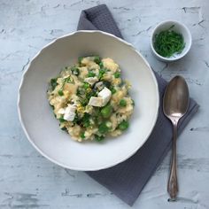 a white bowl filled with pasta and vegetables next to a silver spoon on top of a gray napkin