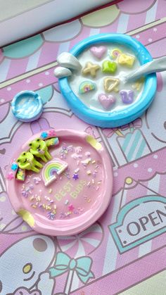 two toys that are sitting on top of a pink and blue tablecloth with unicorns