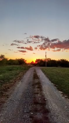 the sun is setting over a dirt road