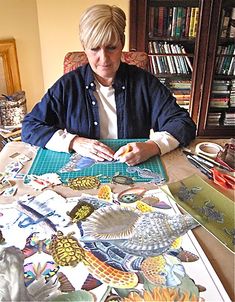 a woman is sitting at a table with many pictures on it, and she has scissors in her hand