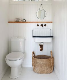 a white toilet sitting next to a sink in a bathroom under a window with a basket on the floor