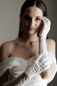 a woman in a white dress is holding her hand up to her face and looking at the camera