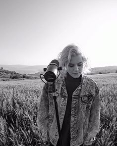 a woman standing in a field with a camera on her shoulder and looking into the distance