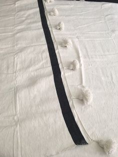 an unmade bed with black and white linens on the bottom, along with tasselled pom - poms