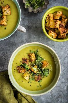 two green bowls filled with soup and croutons on top of a gray table