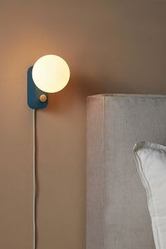 a lamp that is on the side of a wall next to a bed with pillows