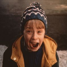 a young boy with his mouth wide open wearing a hat and jacket, standing in the snow