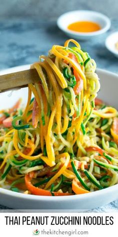 a bowl filled with noodles and vegetables being held by a wooden spoon over the bowl